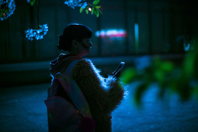 Woman holding phone while standing outdoors at night
