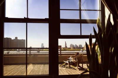 Woman resting on lounge chair at balcony seen through window