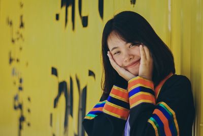 Portrait of smiling young woman standing against yellow wall