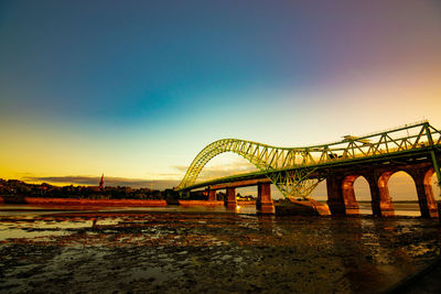 Arch bridge over river against sky during sunset