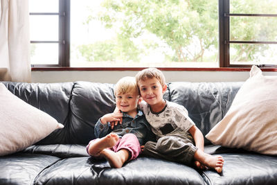 Portrait of cute brothers sitting on sofa at home