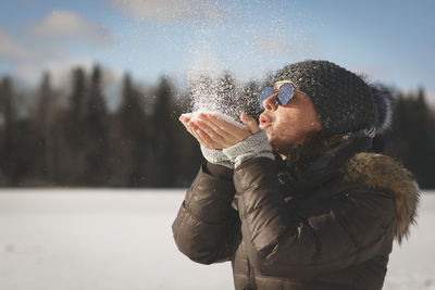 Young woman wearing sunglasses blowing snow