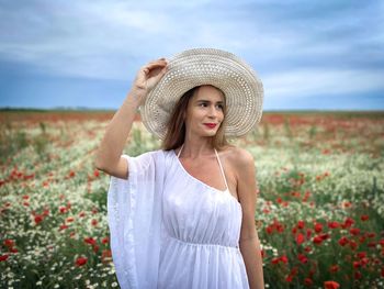Portrait of young woman wearing white dress and hat standing on a field of poppies