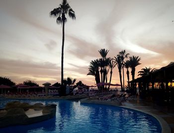 Palm trees by swimming pool against sky during sunset