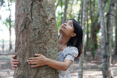 Side view of woman standing by tree trunk in forest