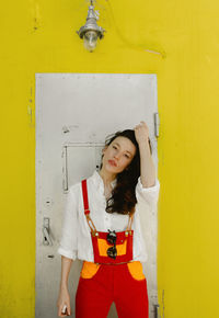 Portrait of young woman standing against yellow wall