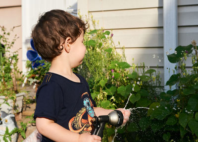 Little boy playing with a watering hose in the backyard