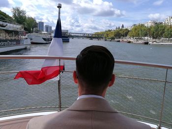 Rear view of man on boat in river against sky