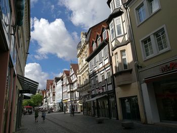 People on street amidst buildings against cloudy sky