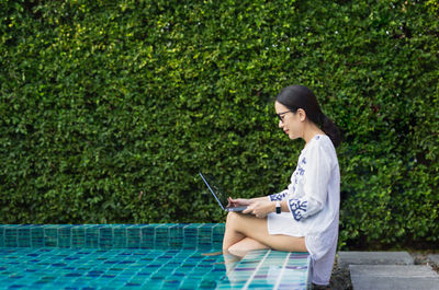 Woman working on laptop computer sitting at poolside on vacation