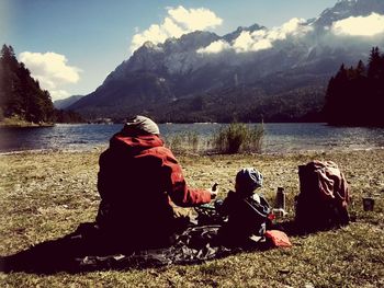 Rear view of woman sitting by lake against mountains