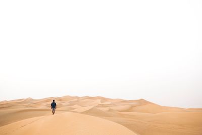 Rear view of man walking at desert against clear sky