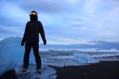 Person standing on ice formation at beach against sky