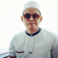 Portrait of young man wearing sunglasses standing against white background