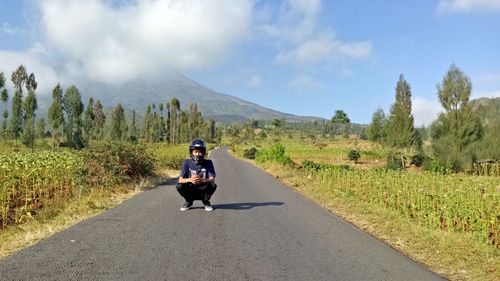 Portrait of man wearing crash helmet while crouching on road against sky