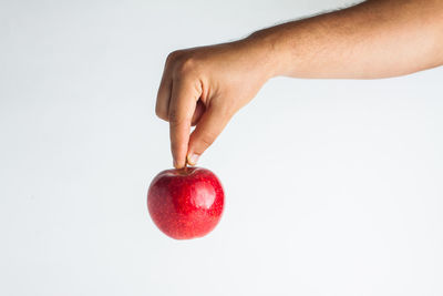 Close-up of hand holding apple against white background