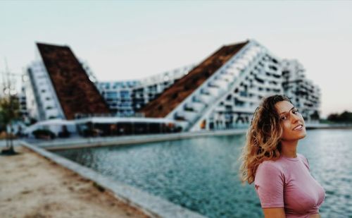 Portrait of woman standing by swimming pool against building