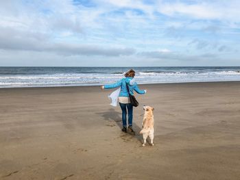 Rear view of woman with dog walking at beach