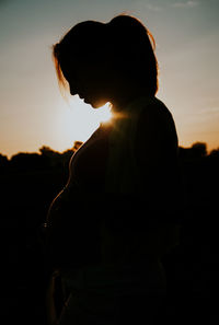 Silhouette of pregnant woman standing against sky during sunset