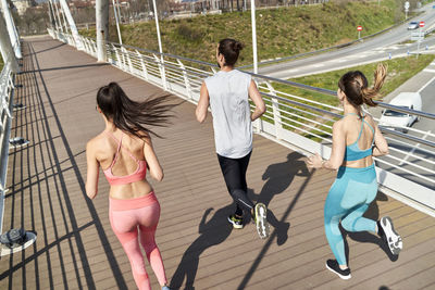 Multi ethnic male and female friends running on bridge during sunny day