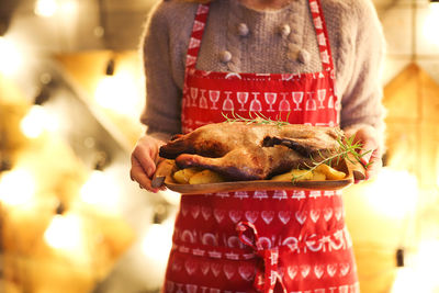 Midsection of woman holding chicken meat at home