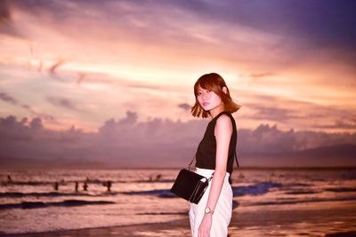 Side view of woman standing at beach against sky during sunset