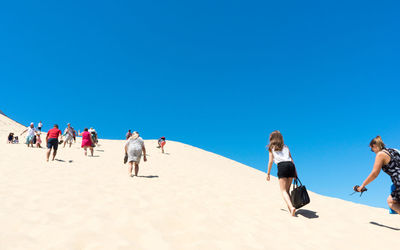 People walking on beach against clear blue sky