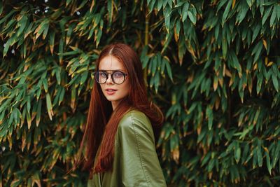 Portrait of young woman standing against plants