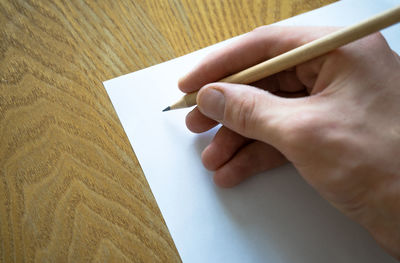 Cropped hand writing on paper with pencil on wooden table