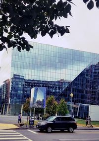 Cars by modern buildings against sky in city