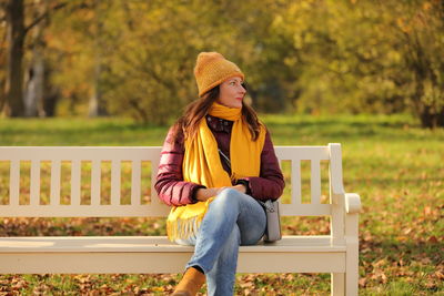 Young woman sitting on bench against trees