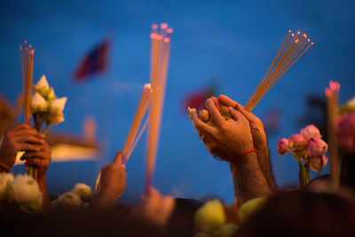 Cropped hands of people holding religious offerings against sky at dusk
