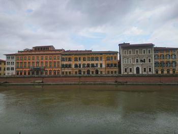 Buildings by river against sky in city