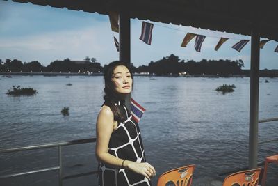 Portrait of woman standing at lakeshore against sky