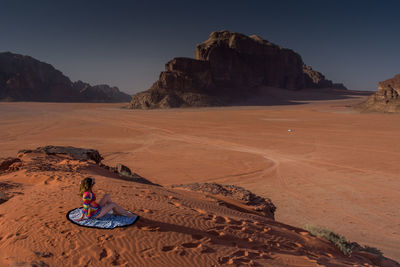 Person sitting on rock by land against sky