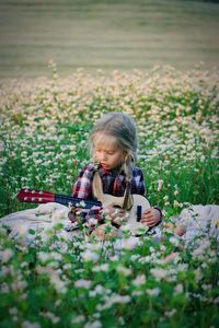 Cute girl holding guitar while sitting amidst plants on field