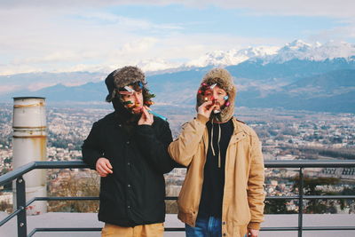 Friends standing on railing in city against sky during winter