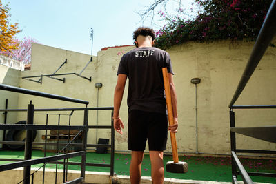 Rear view of young man holding hammer standing outdoors