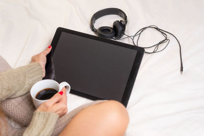 Midsection of person holding coffee cup on bed