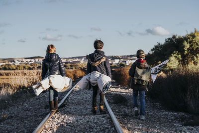 Back view of unrecognizable group of three children hiking in the woods walking in a train track