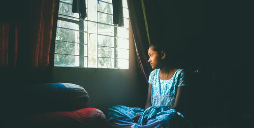 Girl sitting while looking outside through window