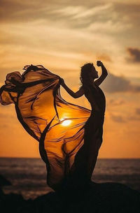 Midsection of woman dancing against sky during sunset