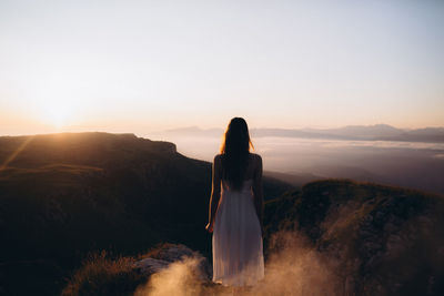 Rear view of young woman standing at field against clear sky