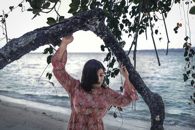Woman standing by tree trunk by sea