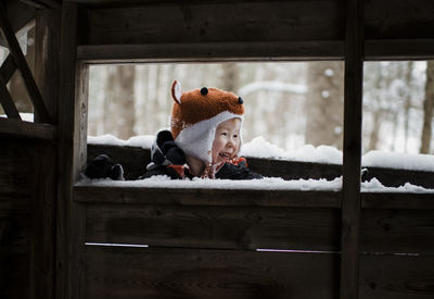 Boy looking away while standing by window during winter