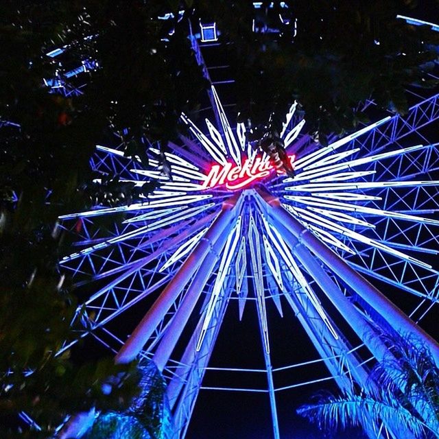 low angle view, built structure, architecture, arts culture and entertainment, night, illuminated, building exterior, amusement park, ferris wheel, amusement park ride, blue, tree, sky, multi colored, outdoors, pattern, no people, clear sky, tall - high, modern