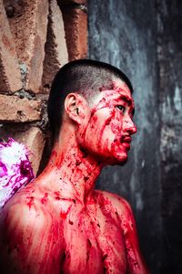 Young man looking away with blood on body while leaning on wall