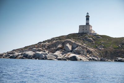 Lighthouse by sea against buildings against clear sky