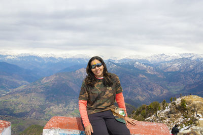 Woman traveler sitting outside kartik swami temple and looking at camera and mountain range