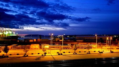 Road by illuminated city against sky at night